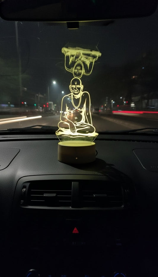 "Illuminated LED 3D illusion figure of Shri Swami Samarth, sitting on a car dashboard at night"LED, 3D illusion, Shri Swami Samarth, car dashboard.alt="Yellow LED light idol of Swami Samarth on a car's dashboard, providing spiritual protection during night driving"